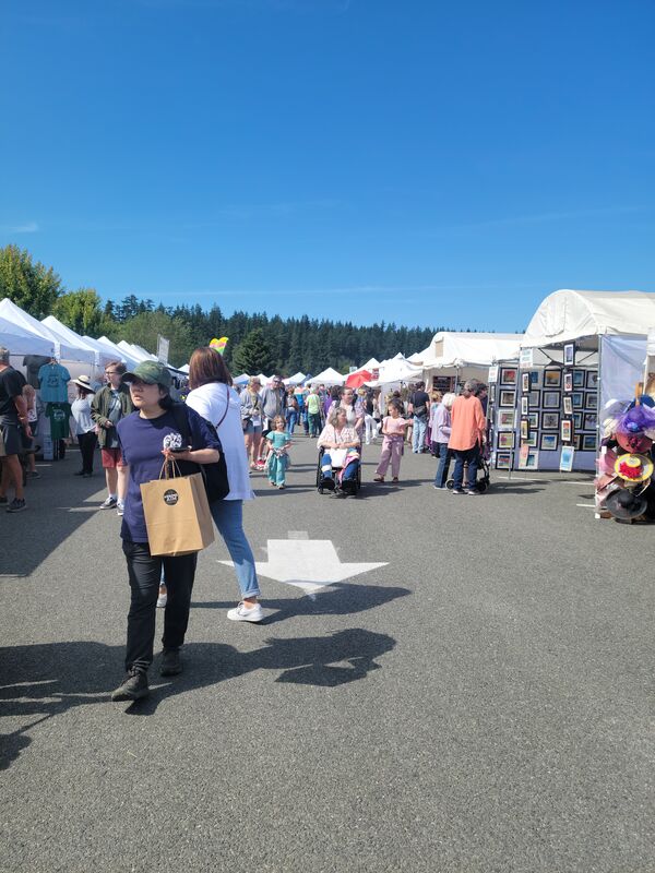 Visitors walking between white vendor tents at the Sequim Lavender Festival street fair